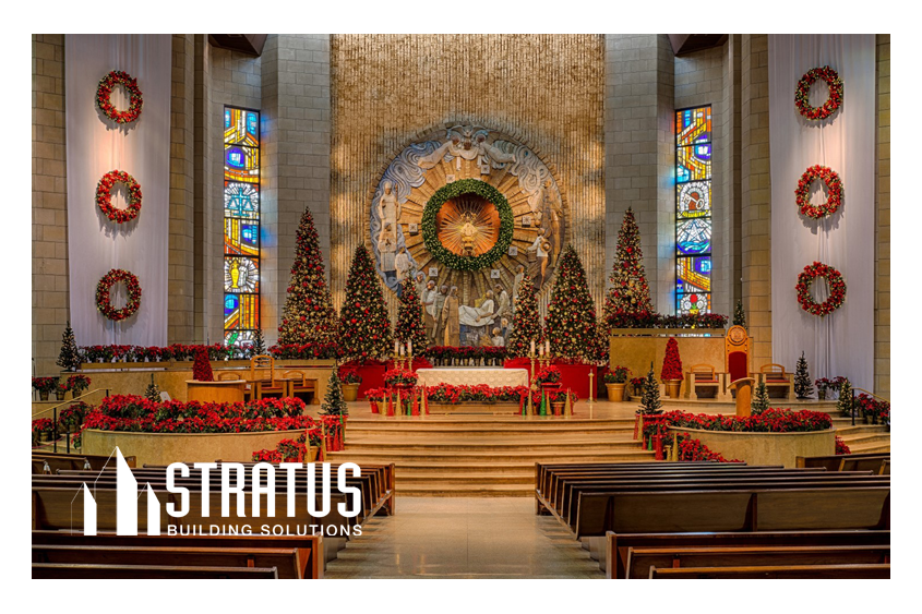 The Interior of a Church Decorated for Christmas with Trees and Wreaths Pictured from Behind the Pews Looking at the Stage